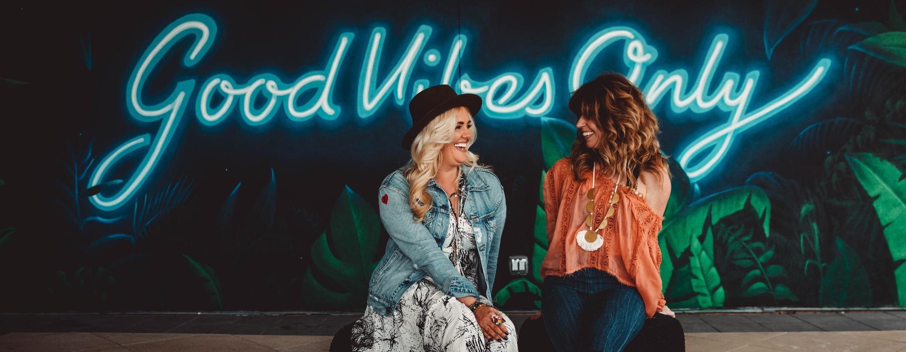 a couple of women sitting on the ground in front of a wall with graffiti